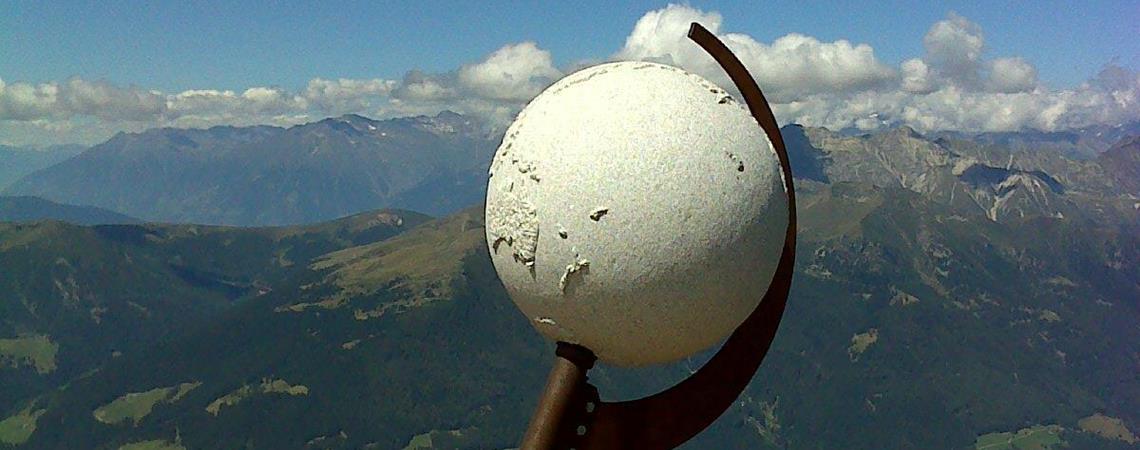 White sphere sculpture on mountain summit with wide valley view and clear sky.