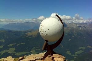 White sphere sculpture on mountain summit with wide valley view and clear sky.