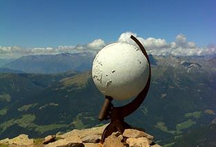Weiße Kugelskulptur auf Berggipfel mit weitem Blick ins Tal und klarem Himmel.
