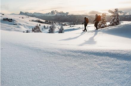 Due escursionisti con le ciaspole camminano in un paesaggio montano innevato al tramonto.