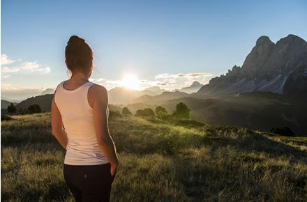 Woman in sportswear looks out at a vast mountain panorama during sunset.