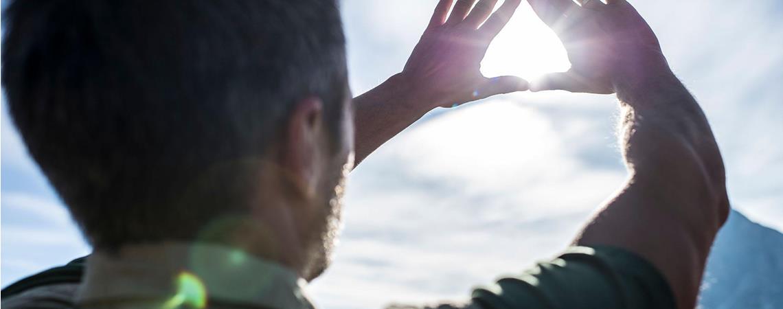 Uomo forma un triangolo con le mani guardando il sole nel cielo luminoso.