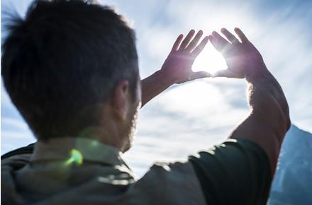 Uomo forma un triangolo con le mani guardando il sole nel cielo luminoso.