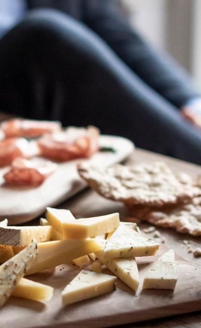 Cheese and speck platter with white wine in a cozy, social setting.
