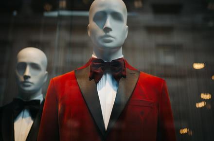 Mannequin wearing red velvet jacket and bow tie in shop window.