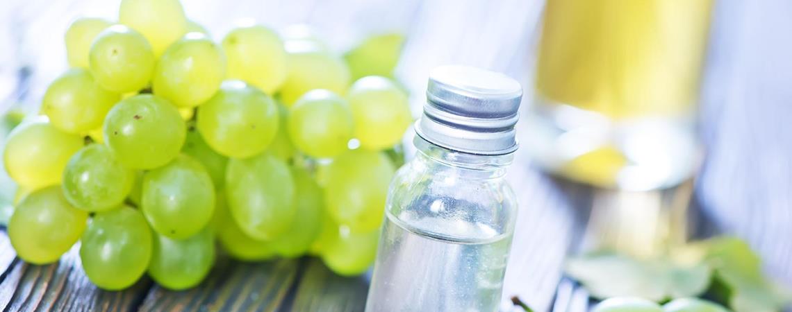 Grüne Weintrauben neben einer kleinen Glasflasche mit Traubenkernöl